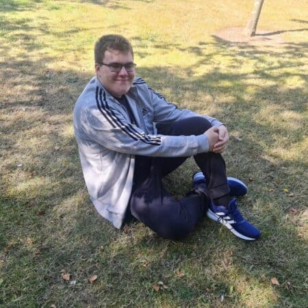 16 year old boy sitting on grass wearing adidas clothing and trainers